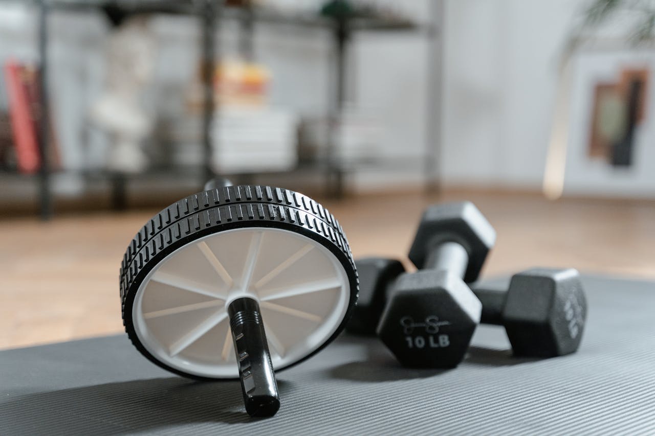 Ab roller and dumbbells on yoga mat, perfect for a home workout routine and healthy lifestyle.